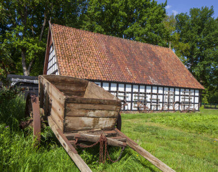 Ein altes Fachwerkhaus das zum Museumshof Rahden gehört, mit einem Wagen aus Holz davor.