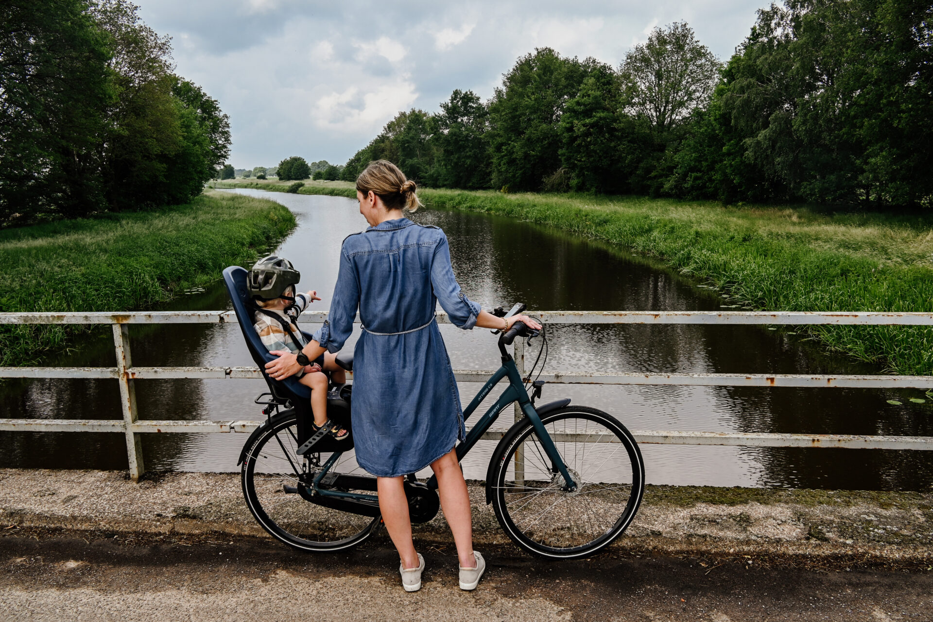 Eine Frau steht auf einer Brücke mit einem Fahrrad, auf dem im Kindersitz ein Kleinkind sitzt.