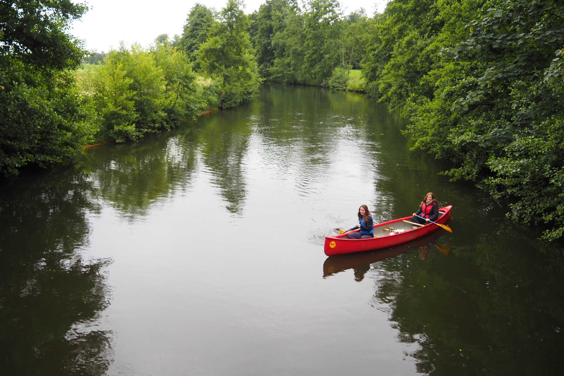Zwei junge Frauen sitzen in einem roten Kanu auf der Hunte und schauen in die Kamera