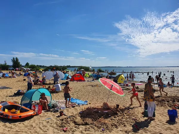 Strandbereich am Dümmer See mit vielen Badegästen, Sonnenschirmen und Zelten bei sonnigem Wetter.