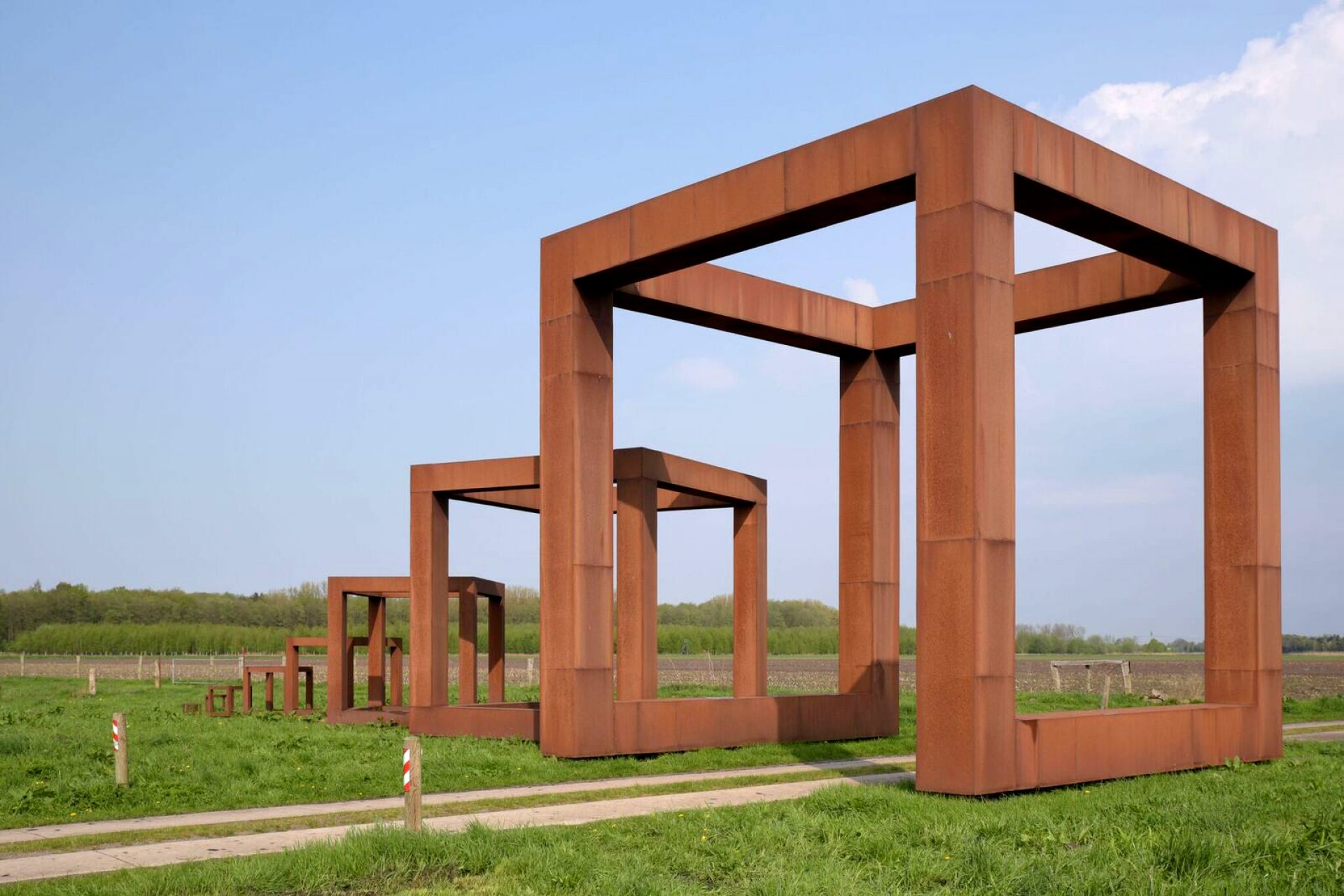 Neun unterschiedlich große, durchlässige Würfel stehen in der weitflächigen Agrarlandschaft.