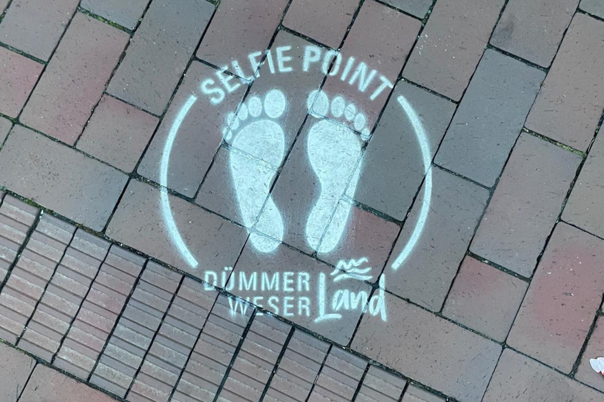 rote Pflastersteine mit einem aufgesprühten Fußabdruck in weißer Farbe mit der Aufschrift Selfie Point über und DümmerWeserLand unter dem Fußabdruck