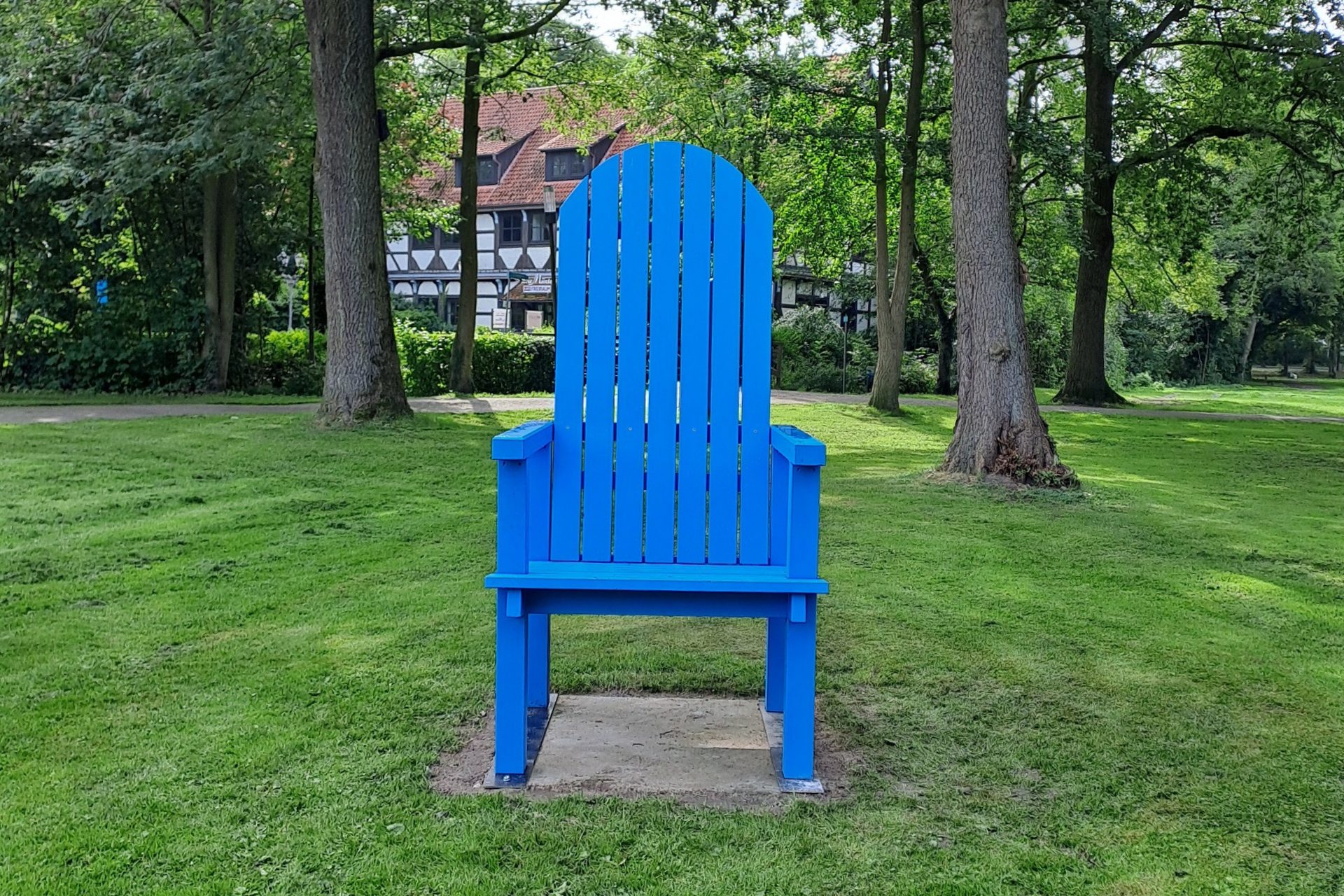 Stuhl Müntepark Ein blauer Stuhl steht auf einer Grasfläche im Müntepark, im Hintergrund sind Bäume.