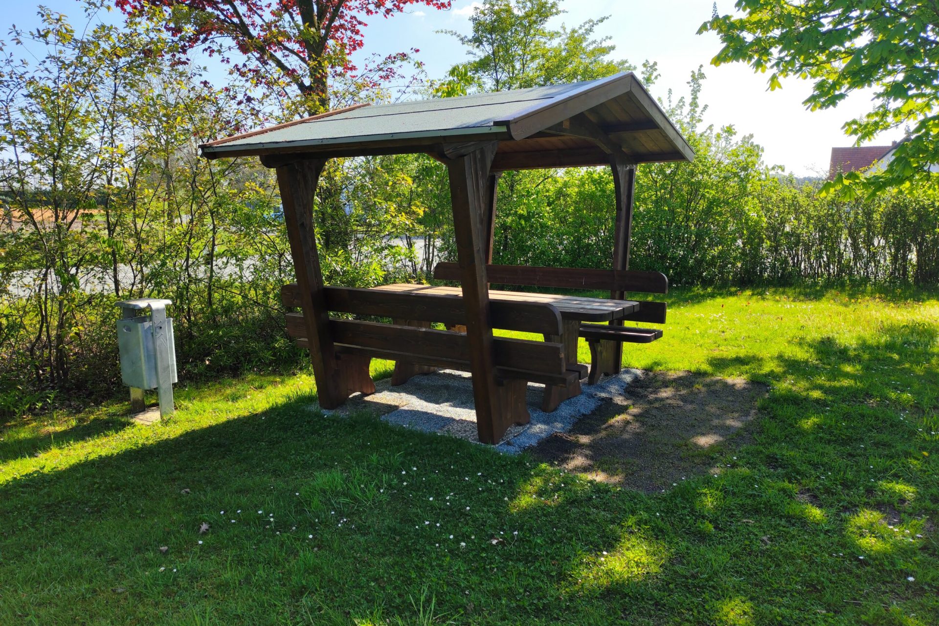 Sundern Überdachter Picknickplatz aus Holz auf einer grünen Rasenfläche vor blühender Hecke